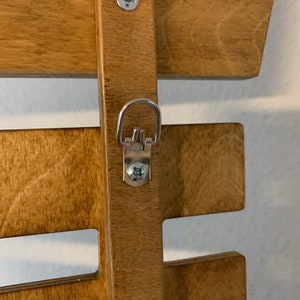 May include: A wooden wall shelf with a metal hanging hook. The shelf is stained a light brown color and has a simple design. The hook is attached to the shelf with a screw.
