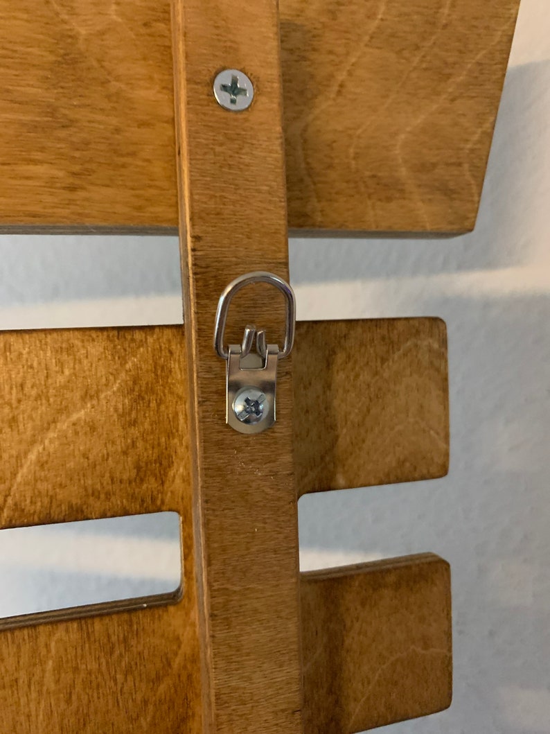 May include: A wooden wall shelf with a metal hanging hook. The shelf is stained a light brown color and has a simple design. The hook is attached to the shelf with a screw.