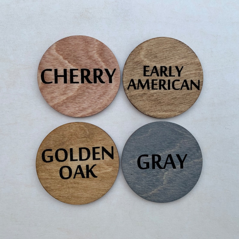 May include: Four round wooden samples with different wood stains. The stains are labeled "Cherry", "Early American", "Golden Oak", and "Gray".