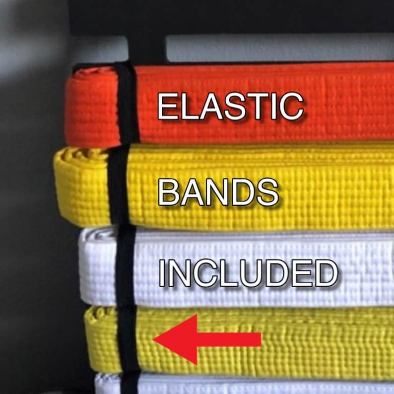May include: A black belt rack with multiple belts hanging on it. The belts are in different colors, including orange, yellow, and white. The text "ELASTIC BANDS INCLUDED" is visible on the rack. An arrow points to the yellow belt.