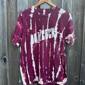 May include: A maroon tie-dye t-shirt with the word "Buzzcocks" printed in white on the front.
