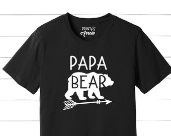 May include: Black t-shirt with white text that reads "Papa Bear" and a white silhouette of a bear walking with an arrow pointing to the right. The text "Print & Arrow" is also visible in white.