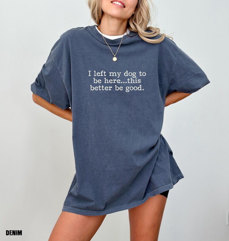 May include: Denim blue t-shirt with the text "I left my dog to be here...this better be good." The shirt has short sleeves and a relaxed fit. The word "DENIM" is printed at the bottom left corner of the image.