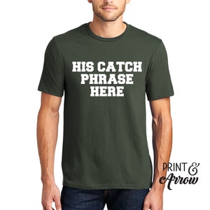 Op de afbeelding: Een donkergroen T-shirt met witte tekst die "HIS CATCH PHRASE HERE" zegt.