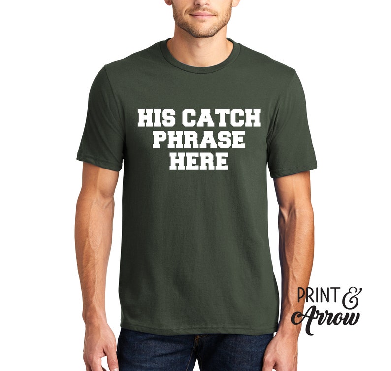 Op de afbeelding: Een donkergroen T-shirt met witte tekst die "HIS CATCH PHRASE HERE" zegt.