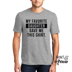 K&ouml;nnte beinhalten: Graues T-Shirt mit schwarzem Text, der "Meine Lieblings-Tochter hat mir dieses Shirt geschenkt." lautet.