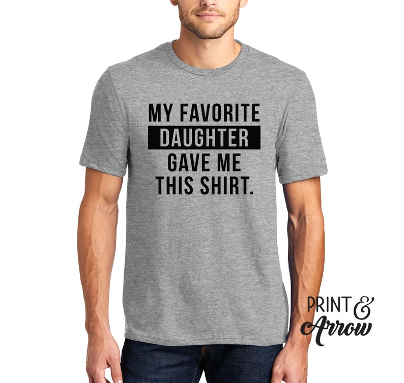 K&ouml;nnte beinhalten: Graues T-Shirt mit schwarzem Text, der "Meine Lieblings-Tochter hat mir dieses Shirt geschenkt." lautet.