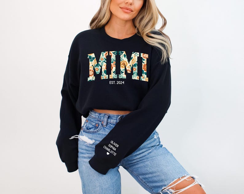 May include: Black cropped sweatshirt with the word "MIMI" in floral print and the text "EST. 2024" below. The sweatshirt has long sleeves and a white heart with the names "OLIVER, SOPHIA, CHARLOTTE" on the left sleeve.