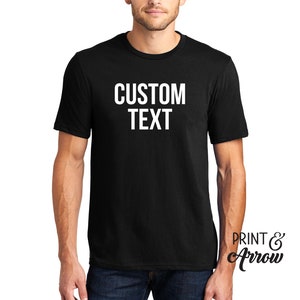Op de afbeelding: Een zwart T-shirt met de tekst "CUSTOM TEXT" in wit op de voorkant.