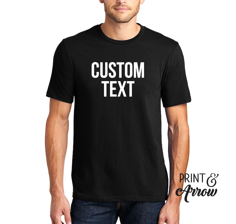 Op de afbeelding: Een zwart T-shirt met de tekst "CUSTOM TEXT" in wit op de voorkant.