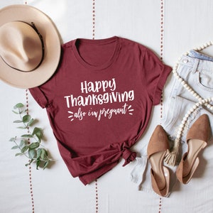 May include: A maroon t-shirt with the text "Happy Thanksgiving also I'm pregnant" in white lettering.