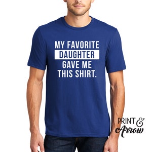 K&ouml;nnte beinhalten: Ein k&ouml;nigsblaues T-Shirt mit wei&szlig;em Text, der "Meine Lieblings-Tochter hat mir dieses Shirt geschenkt." lautet.