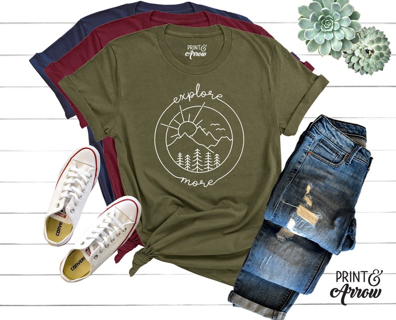 May include: A green t-shirt with a white graphic of a sun, mountains, and trees in a circle with the text "explore more".