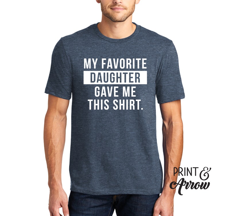 K&ouml;nnte beinhalten: Ein blaues Melange-T-Shirt mit wei&szlig;em Text, der "Meine Lieblings-Tochter hat mir dieses Shirt geschenkt." lautet.