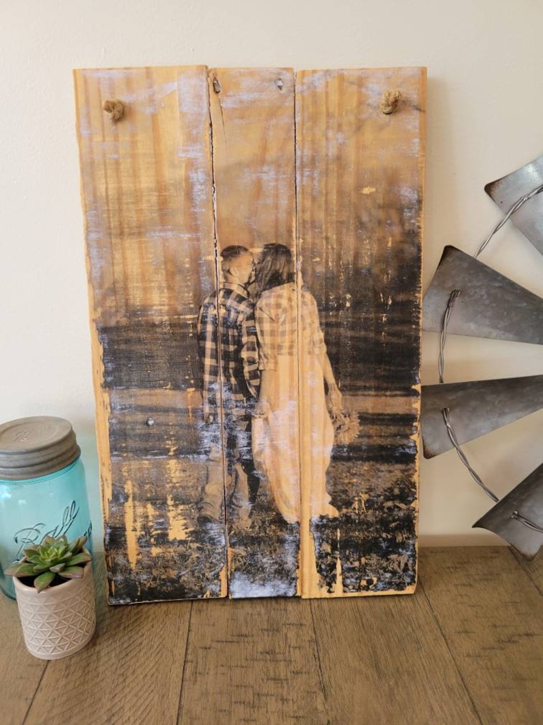 May include: A rustic wooden sign with a black and white photo of a couple kissing. The photo is printed on the wood and has a distressed look. The sign is hanging from two pieces of twine.