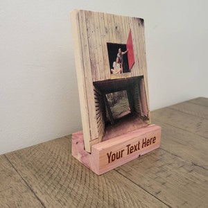 May include: A wooden photo frame with a picture of a couple standing in a doorway. The frame has a wooden stand with the text "Your Text Here" engraved on it.