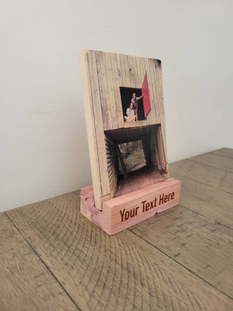 May include: A wooden photo frame with a picture of a couple standing in a doorway. The frame has a wooden stand with the text "Your Text Here" engraved on it.