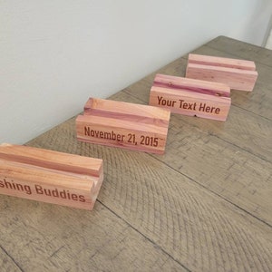 May include: Four wooden blocks with engraved text. The blocks are made of cedar wood and have a natural reddish-brown color. The text on the blocks reads "Fishing Buddies", "November 21, 2015", "Your Text Here", and a blank block.