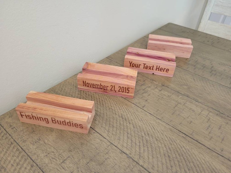 May include: Four wooden blocks with engraved text. The blocks are made of cedar wood and have a natural reddish-brown color. The text on the blocks reads "Fishing Buddies", "November 21, 2015", "Your Text Here", and a blank block.