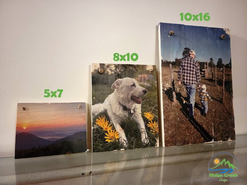 May include: Three wooden photo frames with different sizes and images. The smallest frame is 5x7 inches and shows a sunset over mountains. The middle frame is 8x10 inches and shows a white dog lying in a field of yellow flowers. The largest frame is 10x16 inches and shows a man and a child walking in a field.