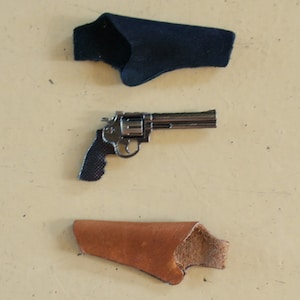 Puede incluir: Un revólver plateado con mango negro y dos fundas, una negra y otra marrón.