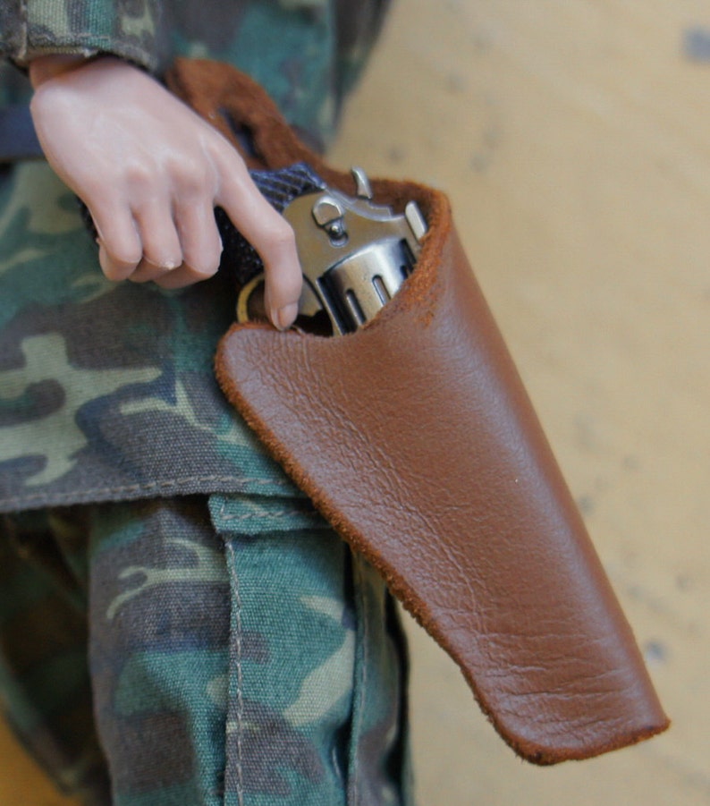 May include: A brown leather holster with a silver handgun inside. The holster is worn on a person's hip.