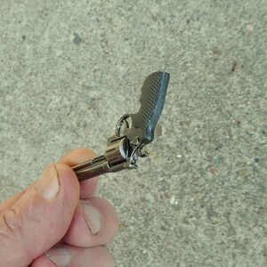 May include: A small, silver-coloured toy gun with a black handle. The gun is held in a person's hand.