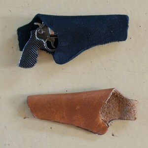 May include: Two leather holsters for a small handgun. One holster is black and the other is brown.