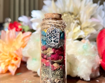 Könnte beinhalten: Eine kleine Glasflasche gefüllt mit getrockneten Kräutern, Blumen und Kristallen. Die Flasche ist mit einem Korken und einem silbernen Anhänger in Form eines Lebensbaums versehen.