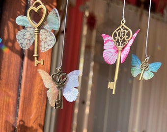 May include: A whimsical mobile with four key-shaped ornaments, each adorned with a delicate butterfly wing. The butterflies are in shades of blue, pink, and green, and the keys are antique gold.