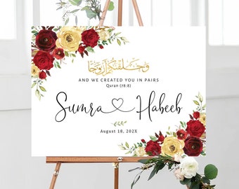 May include: A wedding sign with a floral design in shades of red and yellow. The sign features the Arabic text "وحلفتك اروجا" and the English translation "And we created you in pairs." The names "Sumra" and "Habeeb" are written in cursive script with a heart symbol between them. The date "August 18, 202X" is printed below the names.