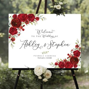 May include: A white wedding welcome sign with red floral borders. The sign reads "Welcome to the Wedding of Ashley & Stephen" and "Pendula Gardens #hashtagHere | 8.16.2025".