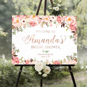 K&ouml;nnte beinhalten: Ein wei&szlig;es Willkommens-Schild mit rosa floralen R&auml;ndern und dem Text "WELCOME TO Amanda's BRIDAL SHOWER 56 Days until she says 'I do' August 21, 2026"