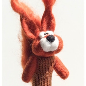 May include: A red felt finger puppet of a squirrel with a white face and black nose. The squirrel is wearing a brown knitted sweater.