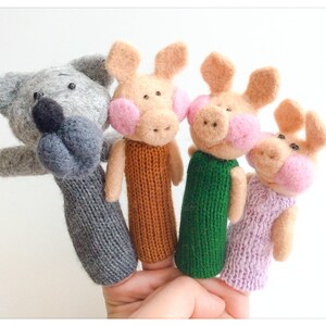 Peut inclure: Un ensemble de marionnettes à doigts représentant un loup gris et trois cochons roses. La marionnette du loup a un corps en tricot gris et un nez noir. Les marionnettes des cochons ont des corps en tricot orange, vert et violet.