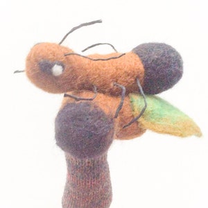 May include: A brown and black felt finger puppet shaped like a bee with green and yellow wings.