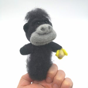 May include: A black and gray felt finger puppet of a gorilla holding a yellow banana.