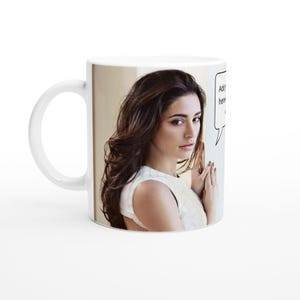 Könnte beinhalten: Weiße Keramiktasse mit einem Foto einer Frau mit langen braunen Haaren. Die Frau trägt ein weißes Oberteil und schaut in die Kamera. Der Text "In den Warenkorb..." befindet sich in einer Sprechblase über ihrem Kopf.