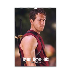 Puede incluir: Un calendario de pared con una foto de Ryan Reynolds. El calendario tiene un fondo negro y el texto "Ryan Reynolds Wall Calendar" está impreso en blanco en la parte inferior.
