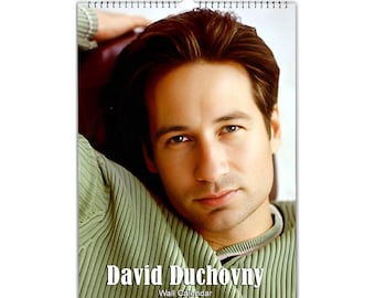 Op de afbeelding: Wandkalender met een kleurenfoto van David Duchovny. Hij draagt een groene geribbelde trui. De tekst "David Duchovny" en "Wall Calendar" zijn wit gedrukt onderaan de kalender. Metalen spiraalbinding.