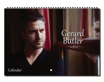 May include: A calendar featuring a black and white photo of Gerard Butler. The photo shows Butler looking directly at the camera with a serious expression. The background is a blurry image of a window with red curtains.