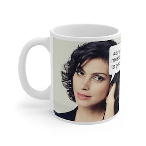 May include: White ceramic coffee mug featuring a photo of a woman with dark hair and a speech bubble that says "Add your message to personalise".