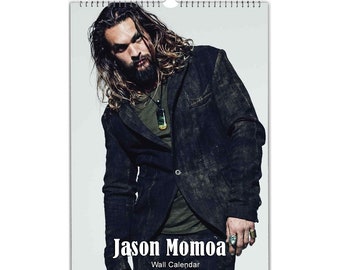 May include: A wall calendar featuring a photo of Jason Momoa. The photo shows him wearing a black jacket, a green shirt, and a necklace. The text "Jason Momoa" and "Wall Calendar" is printed below the photo.