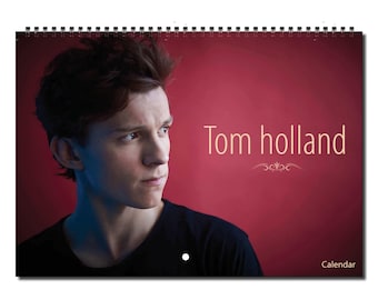 Könnte beinhalten: Ein Kalender mit einem Nahaufnahmeporträt von Tom Holland vor rotem Hintergrund. Der Text "Tom Holland" ist in hellbrauner Schrift über seinem Kopf geschrieben.
