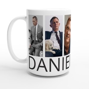 May include: White ceramic mug with a collage of images of Daniel Craig. The mug has the word "DANIEL" printed in black at the bottom.