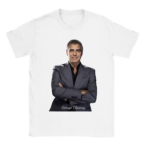 Puede incluir: Una camiseta blanca con una foto de George Clooney con un traje gris y una camisa negra. El texto "George Clooney" está impreso debajo de la foto.