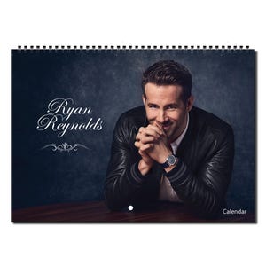 Puede incluir: Un calendario con una foto de Ryan Reynolds. La foto lo muestra con una chaqueta de cuero negra y mirando a la cámara con una sonrisa. El texto "Ryan Reynolds" está escrito en letras blancas en cursiva en la parte superior de la imagen.