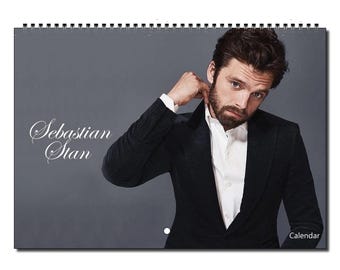 May include: A calendar featuring a photo of Sebastian Stan. He is wearing a black suit jacket and a white shirt. The background is a gray wall. The text "Sebastian Stan" is written in white cursive on the left side of the image. The text "Calendar" is written in white on the bottom right side of the image.