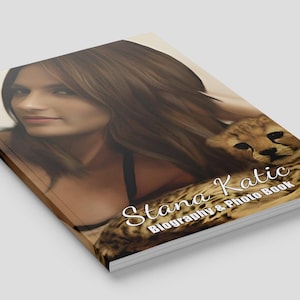 May include: A book titled "Stana Katic Biography & Photo Book" featuring a woman and a cheetah cub. The cover has a light background with the title in white script.