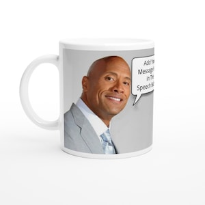 Può includere: Tazza in ceramica bianca con un'immagine di Dwayne Johnson, noto anche come The Rock, con un fumetto che dice "Aggiungi il tuo messaggio qui nella bolla del discorso".